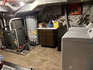 Laundry area featuring water heater, washer and dryer, light tile floors, brick wall, and heating utilities