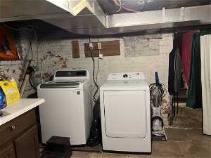 Laundry room featuring dark tile flooring, independent washer and dryer, and brick wall