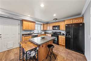 Kitchen with a center island, sink, black appliances, a breakfast bar, and ornamental molding