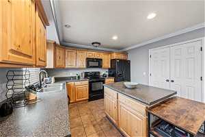 Kitchen with sink, a center island, crown molding, light tile floors, and black appliances