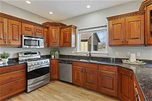 Kitchen featuring stainless steel appliances, light wood-type flooring, dark stone countertops, and sink