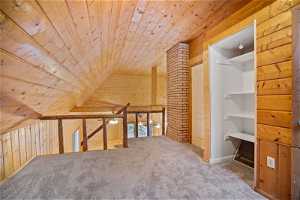 Additional living space featuring light carpet, wooden walls, brick wall, vaulted ceiling, and wooden ceiling
