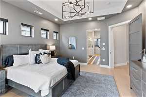 Bedroom featuring a tray ceiling, ensuite bath, light wood-type flooring, and an inviting chandelier
