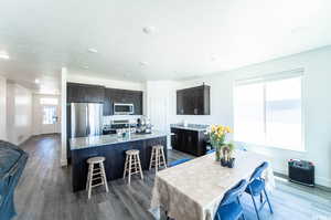 Kitchen with wood-type flooring, appliances with stainless steel finishes, a kitchen bar, and light stone counters