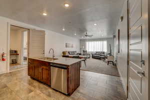 Kitchen featuring light carpet, sink, dishwasher, a center island with sink, and ceiling fan