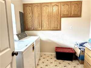 Laundry room with washing machine and dryer, light tile floors, and cabinets