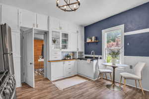 Kitchen with white cabinetry, stainless steel refrigerator, range, wood-style floors