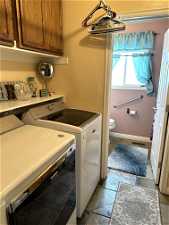 Clothes washing area featuring washer and clothes dryer, light tile floors, and cabinets