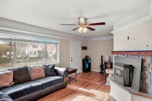 Living room with light wood-type flooring, a wood stove, and ceiling fan