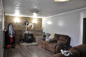 Living room with a textured ceiling, dark hardwood / wood-style flooring, a wood stove, and brick wall