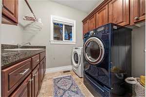 Laundry area with sink, light tile flooring, washing machine and clothes dryer, and cabinets, just off mudroom.