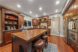 Kitchen featuring sink, a kitchen island, wooden counters, stainless steel appliances, and dark hardwood / wood-style flooring