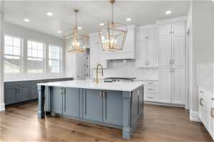 Kitchen with tasteful backsplash, light hardwood / wood-style flooring, white cabinetry, and a center island with sink