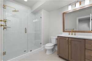 Bathroom featuring a shower with shower door, vanity, tile floors, and toilet