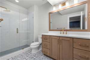 Bathroom featuring a shower with door, vanity, tile floors, and toilet