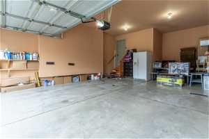 Garage with white refrigerator with ice dispenser and a garage door opener