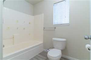 Bathroom with toilet, shower / washtub combination, and hardwood / wood-style flooring