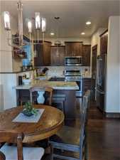 Kitchen featuring dark brown cabinetry, stainless steel appliances, decorative light fixtures, backsplash, and dark hardwood / wood-style floors