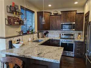 Kitchen featuring sink, dark brown cabinetry, stainless steel appliances, backsplash, and a kitchen breakfast bar