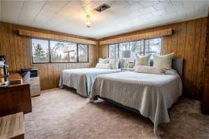 Carpeted bedroom featuring multiple windows and wood walls