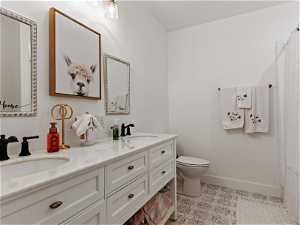 Bathroom featuring toilet, double sink, vanity with extensive cabinet space, and tile flooring