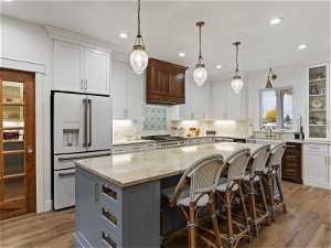 Kitchen with premium range hood, light hardwood / wood-style floors, a center island, high end white refrigerator, and white cabinets