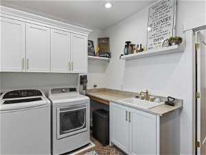 Laundry area with washer and clothes dryer, cabinets, and sink