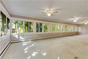 Unfurnished sunroom featuring ceiling fan, a healthy amount of sunlight, and a baseboard heating unit