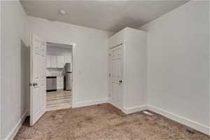 Unfurnished bedroom with light colored carpet and stainless steel fridge