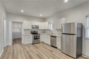 Kitchen with light hardwood / wood-style flooring, white cabinets, sink, and appliances with stainless steel finishes