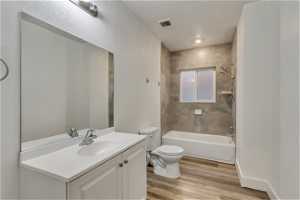 Full bathroom with toilet, tiled shower / bath, oversized vanity, and wood-type flooring