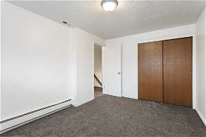 Unfurnished bedroom with dark carpet, a closet, baseboard heating, and a textured ceiling
