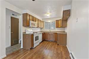 Kitchen with a baseboard heating unit, white appliances, a textured ceiling, and light hardwood / wood-style floors