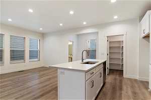 Kitchen with dishwasher, white cabinets, hardwood / wood-style flooring, sink, and a kitchen island with sink