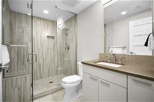 Bathroom with toilet, an enclosed shower, vanity with extensive cabinet space, tile flooring, and backsplash