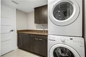 Clothes washing area featuring light tile floors, stacked washer and dryer, sink, and cabinets