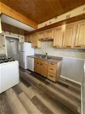 Kitchen featuring dark wood-type flooring, white appliances, wood ceiling, and sink