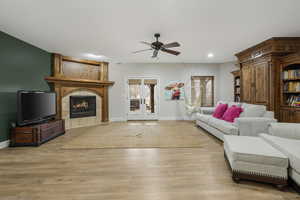 Living room with ceiling fan, a tiled fireplace, french doors, and light hardwood / wood-style flooring