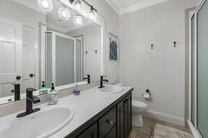 Bathroom with an inviting chandelier, a shower with shower door, tile flooring, dual vanity, and toilet