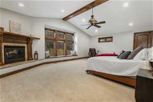 Bedroom featuring lofted ceiling with beams, a tile fireplace, ceiling fan, and light colored carpet