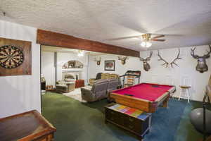 Recreation room featuring beamed ceiling, dark colored carpet, ceiling fan, a textured ceiling, and billiards