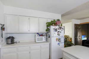 Kitchen with white appliances, a textured ceiling, and white cabinetry