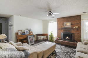 Living room with a textured ceiling, ceiling fan, a brick fireplace, and brick wall