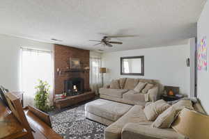 Living room featuring a fireplace, ceiling fan, plenty of natural light, and a textured ceiling