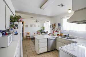 Kitchen with an inviting chandelier, dishwasher, sink, light tile floors, and kitchen peninsula