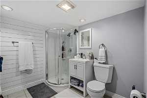 Bathroom featuring toilet, an enclosed shower, wood walls, tile floors, and large vanity
