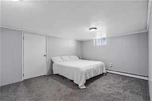 Bedroom featuring dark carpet, baseboard heating, a textured ceiling, and crown molding