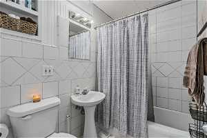 Full bathroom featuring toilet, shower / bath combo with shower curtain, tile walls, and sink