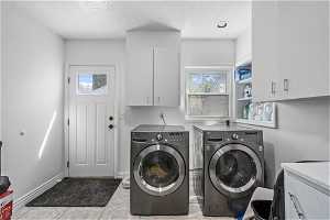Clothes washing area with washing machine and clothes dryer, cabinets, and light tile flooring