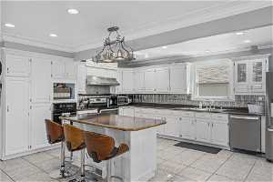 Kitchen with a chandelier, appliances with stainless steel finishes, white cabinets, tasteful backsplash, and a kitchen island
